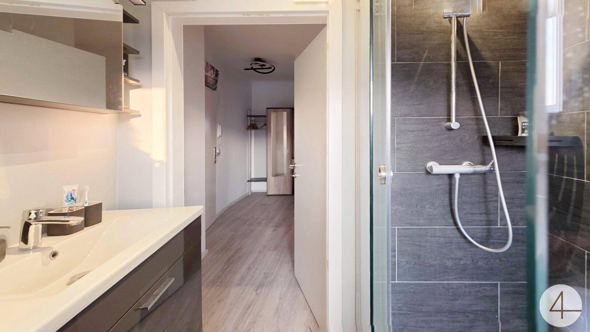Badezimmer mit moderner Dusche und Waschbecken, angrenzend an einen Flur.