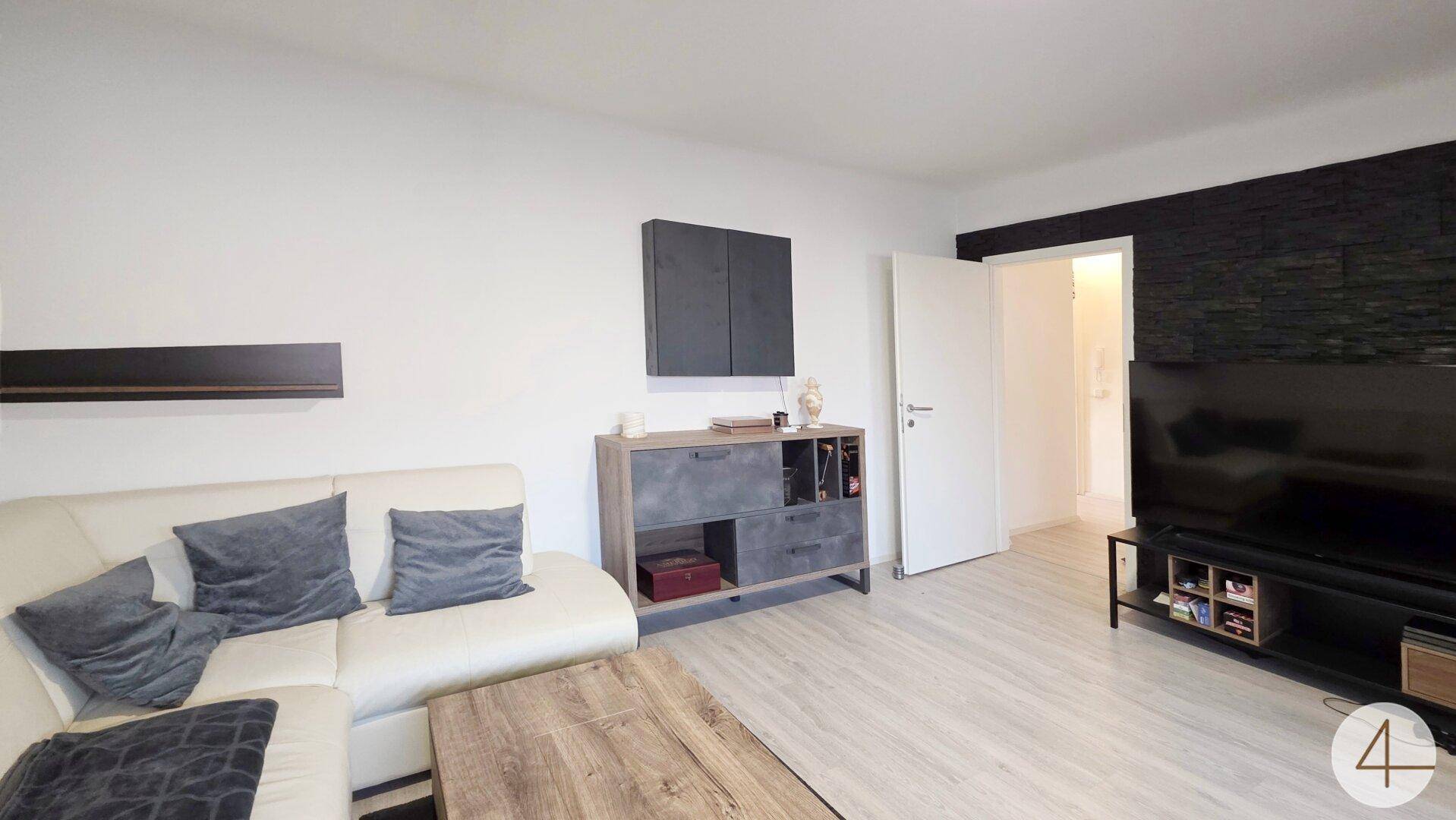 Modern eingerichtetes Wohnzimmer mit heller Couch, Holztisch und dunkler Akzentwand.