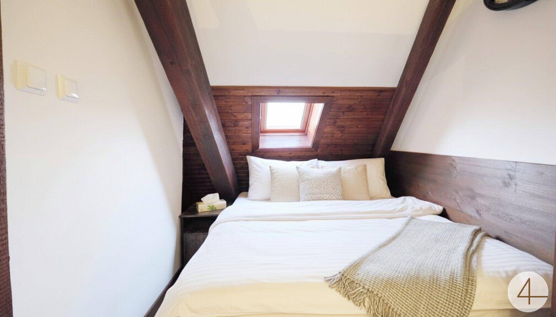 Gemütliches Schlafzimmer im Dachgeschoss mit Holzbalken und Dachfenster.