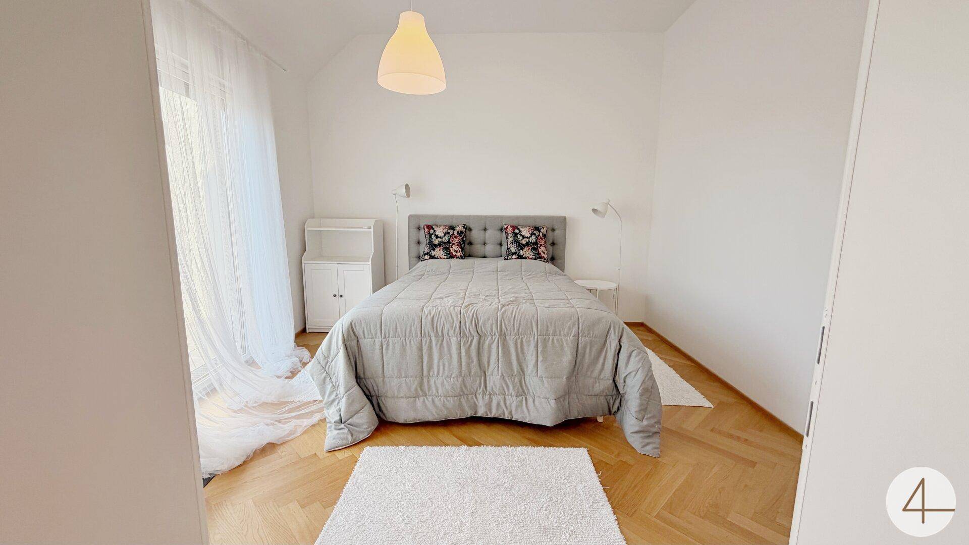 Gemütliches Schlafzimmer mit Doppelbett, Parkettboden und viel Tageslicht.