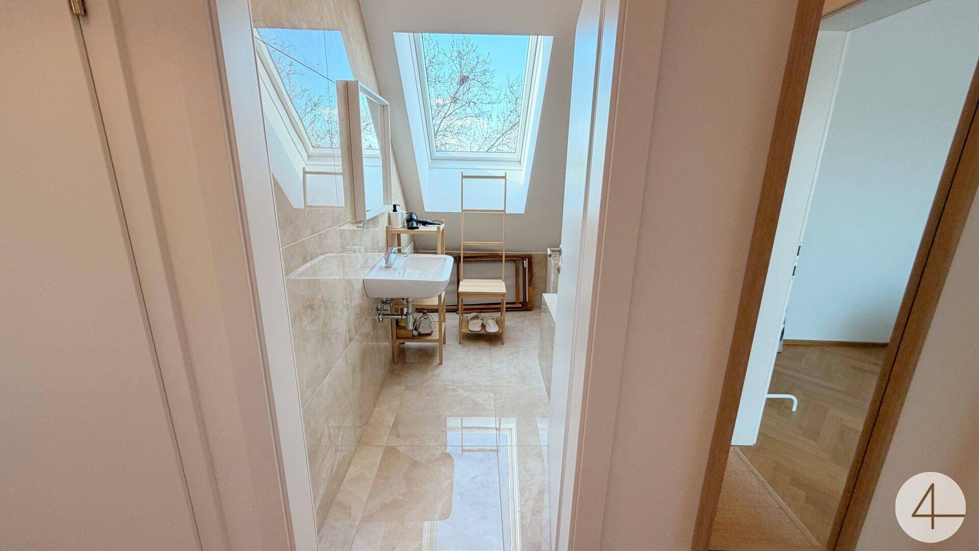 Modernes Badezimmer mit Waschbecken, Spiegel und Dachfenster für natürliches Licht.