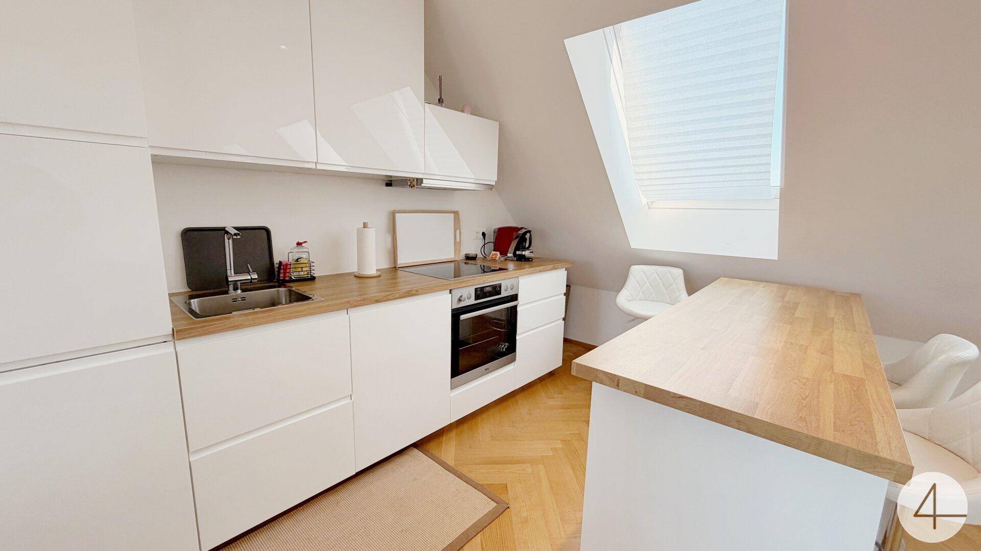 Moderne weiße Küche mit Holz-Arbeitsplatte, Dachfenster und integrierten Geräten.