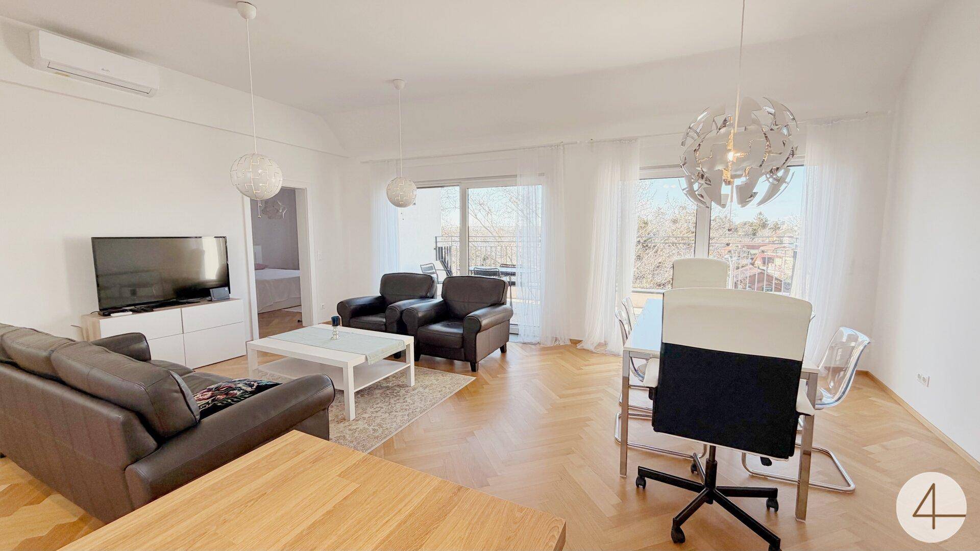 Geräumiger Wohn-Essbereich mit Parkettboden, großen Fenstern und Zugang zum Balkon.