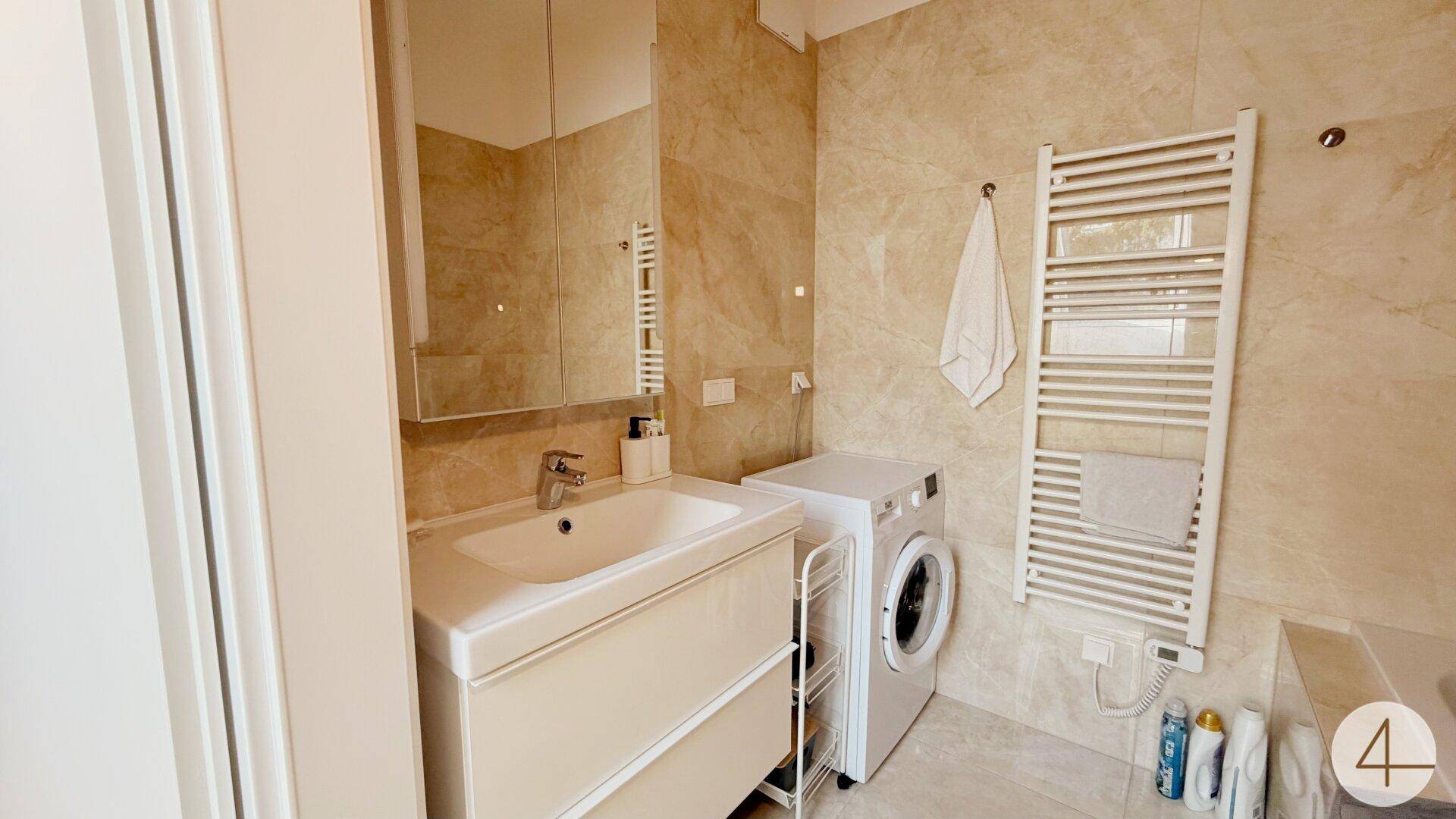 Modernes Badezimmer mit beigefarbenen Fliesen, Einzelwaschbecken und beheiztem Handtuchhalter.