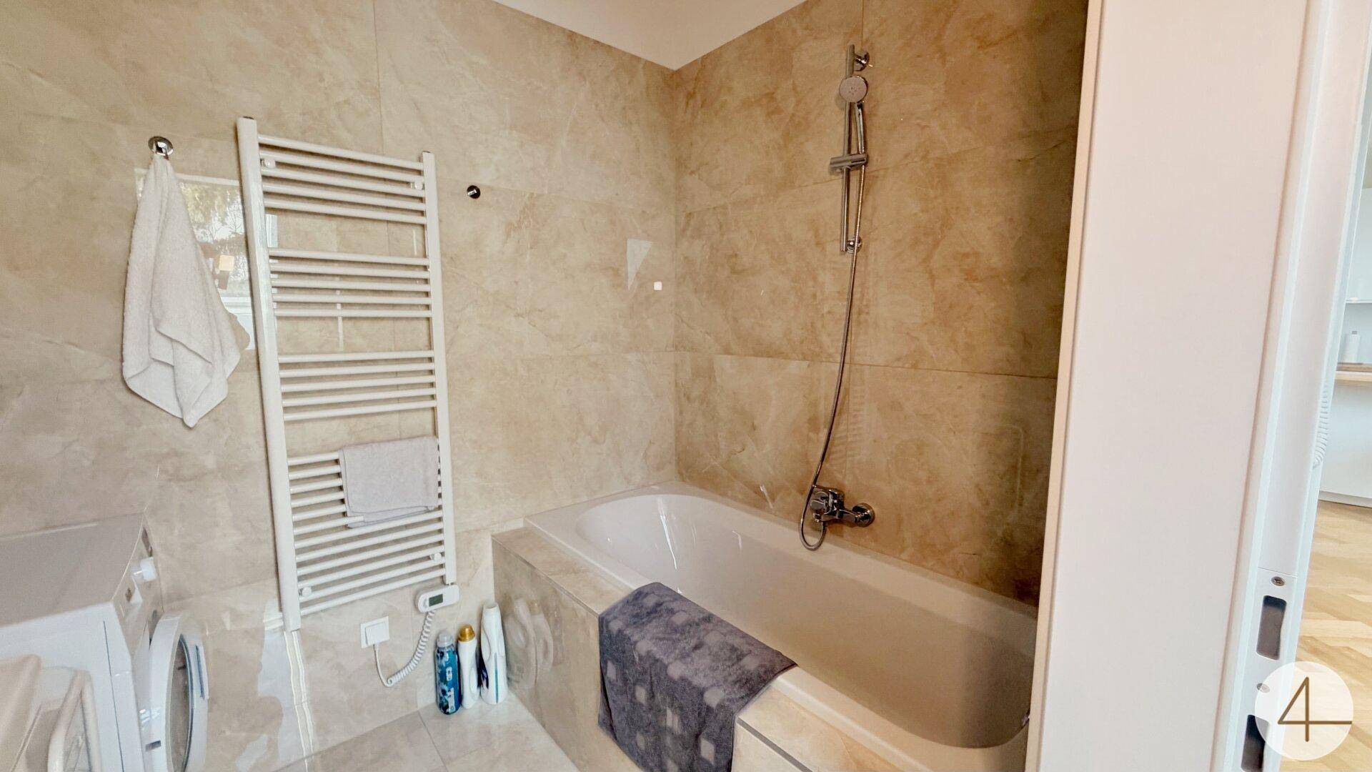 Helles Badezimmer mit Badewanne, beigefarbenen Fliesen und Handtuchheizkörper.