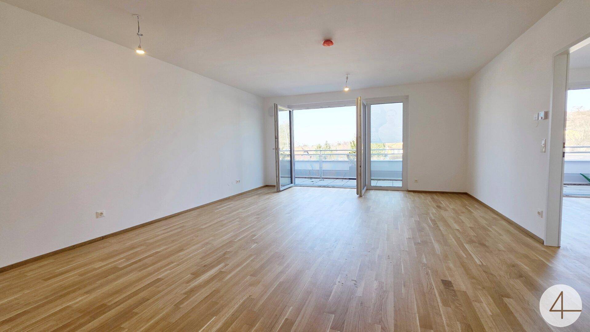 Geräumiges, helles Wohnzimmer mit Parkettboden und breiter Fensterfront zum Außenbereich.