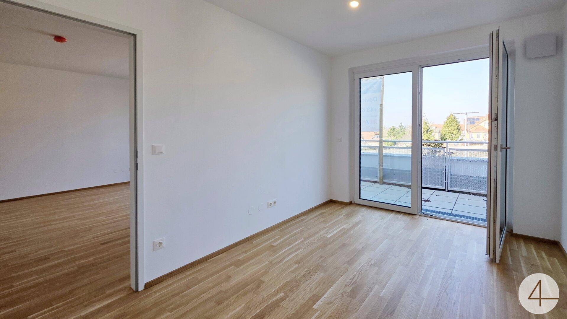 Heller Raum mit Parkettboden und Zugang zu einem Balkon, der viel Tageslicht hereinlässt.