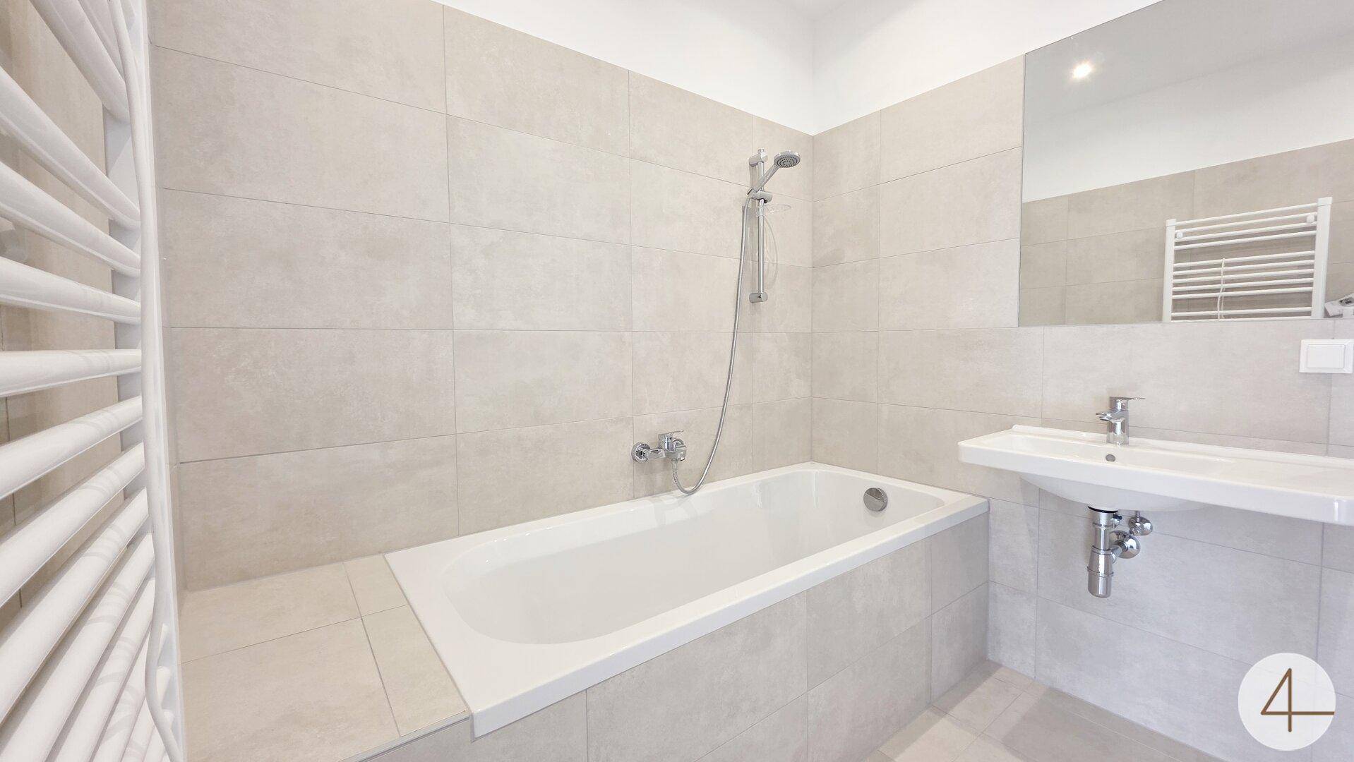 Modernes Badezimmer mit Badewanne, Waschbecken, großem Spiegel und beheiztem Handtuchhalter.