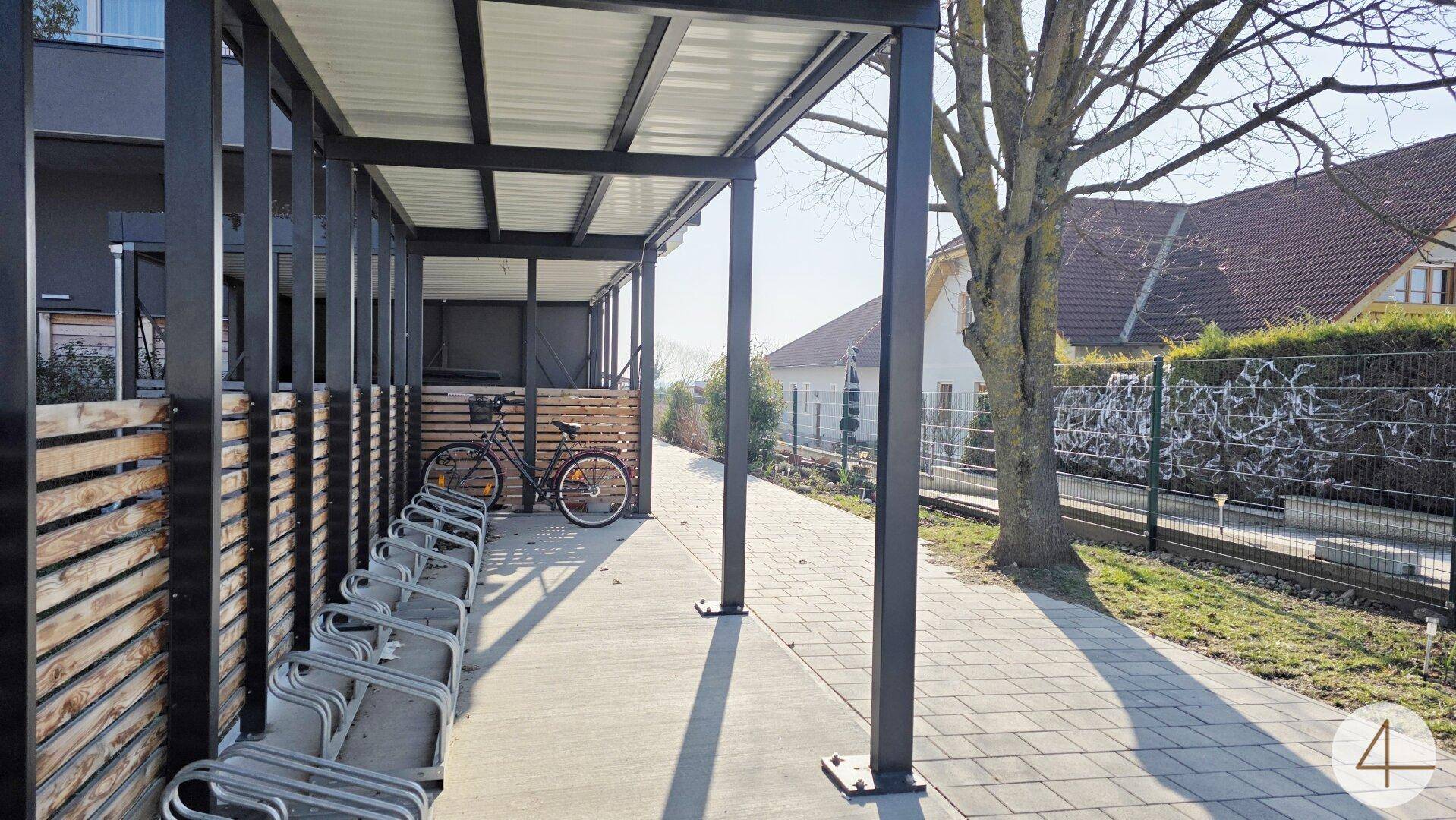 Überdachter Fahrradabstellplatz mit mehreren Ständern neben dem Gebäude.