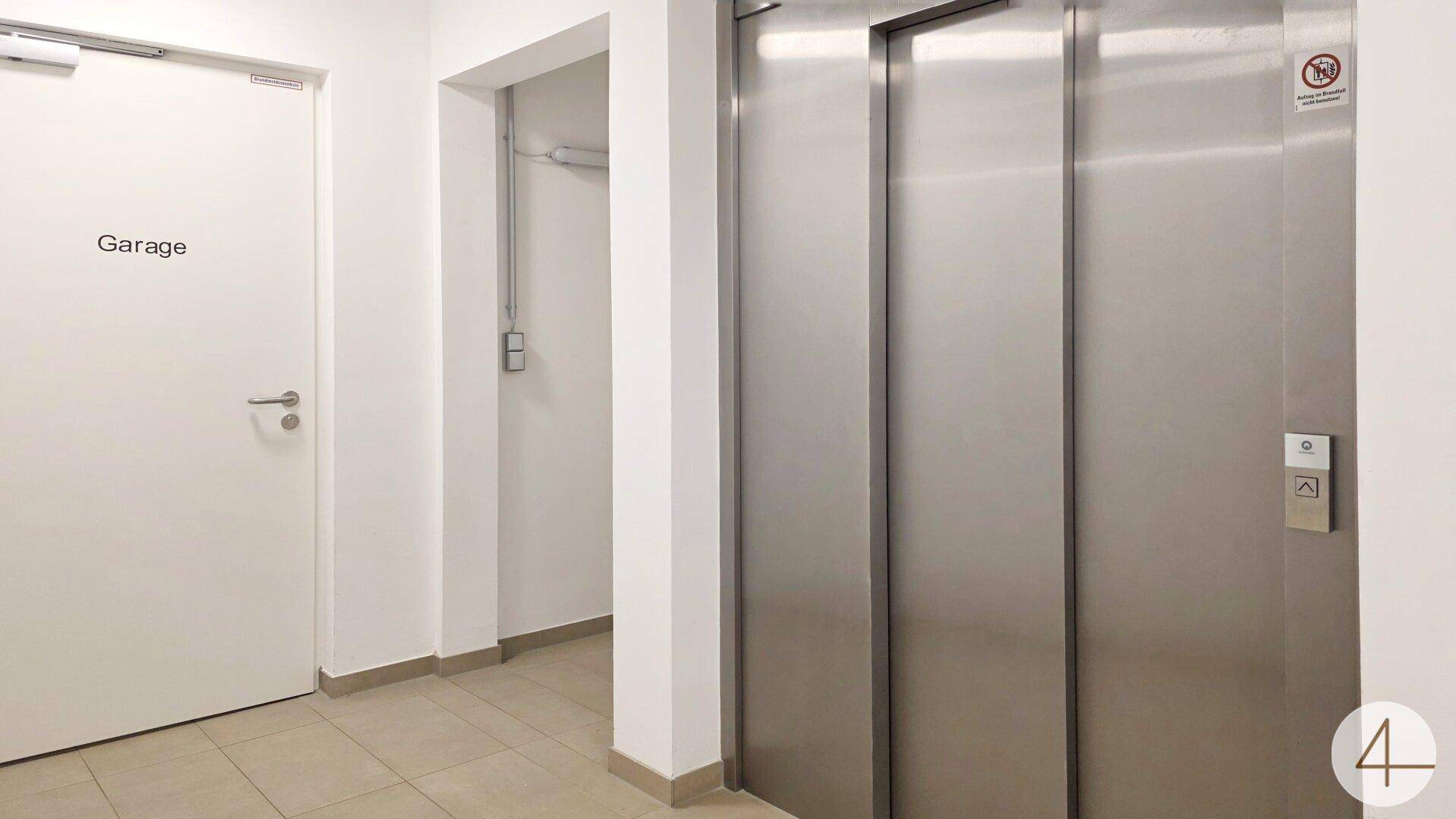 Moderner Aufzug und Zugangstür zur Tiefgarage in einem hellen Flurbereich.