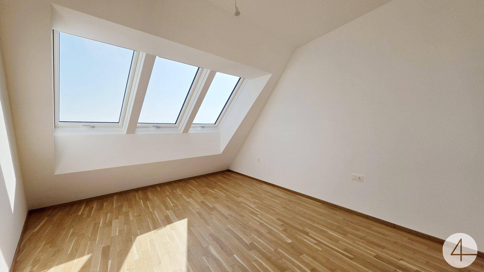 Geräumiges Dachzimmer mit schrägen Wänden, Parkettboden und drei großen Dachfenstern für viel Licht.
