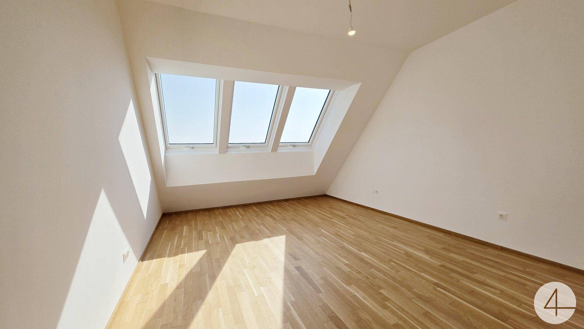 Helles Dachzimmer mit Parkettboden und schrägen Wänden, ideal für ein Schlafzimmer oder Büro.