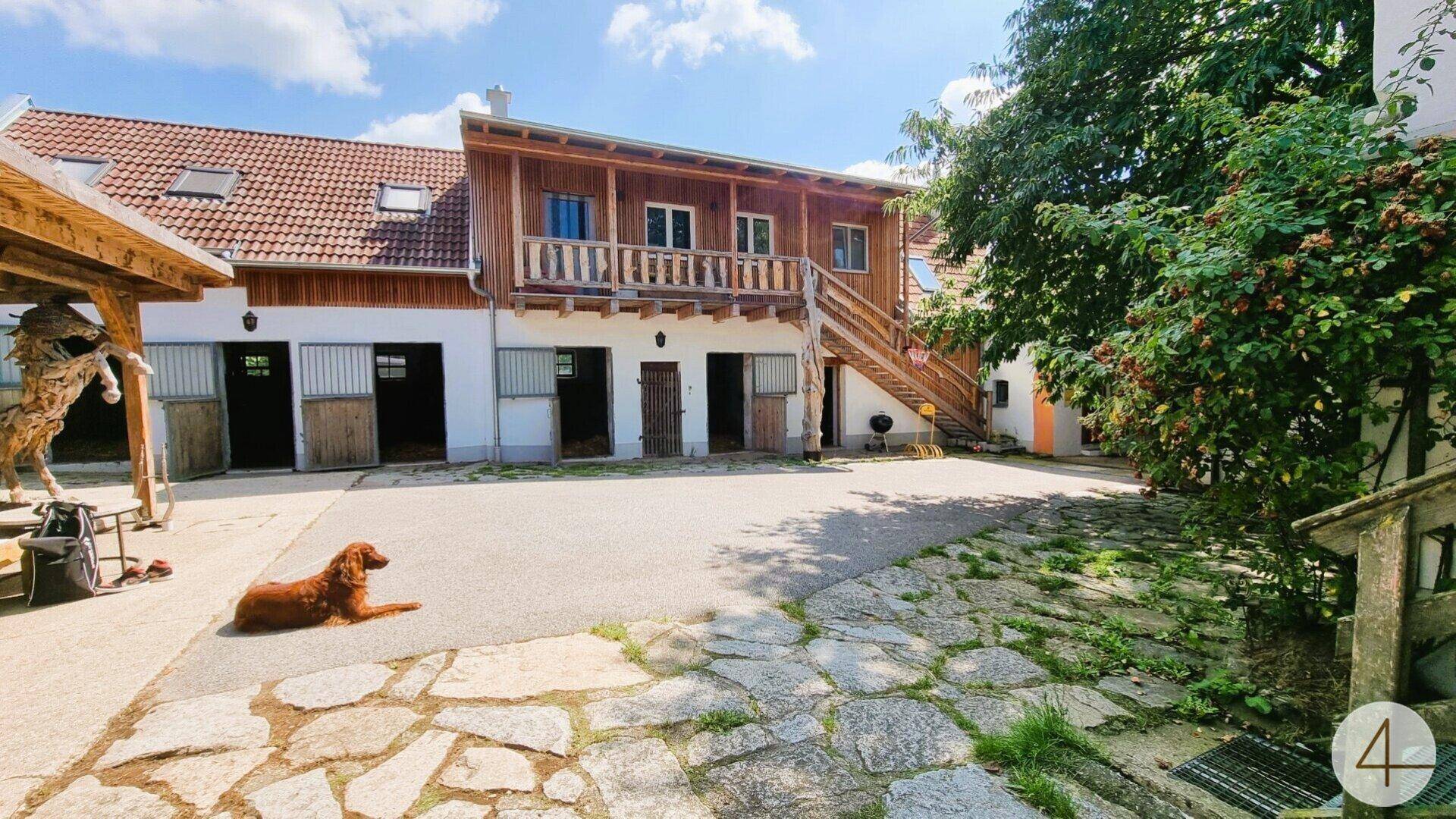 Idyllischer Innenhof mit rustikalem Steinboden, Stallungen und einem Holzgebäude mit Balkon.