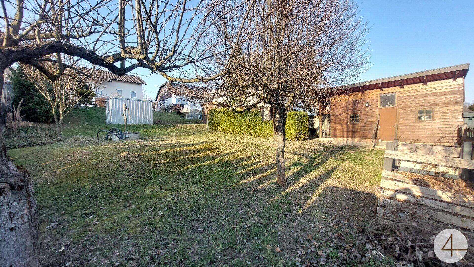 Gartenbereich mit Rasen, Bäumen und einem Holzschuppen, bietet Stauraum und eine angenehme Grünfläche.