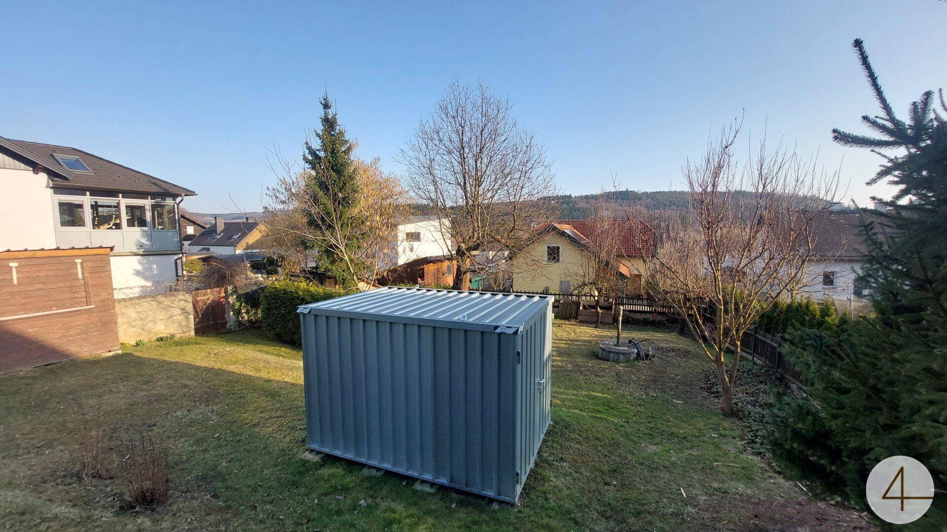 Garten mit Rasenfläche, einem modernen Metallschuppen und weitem Blick auf die grüne Landschaft.