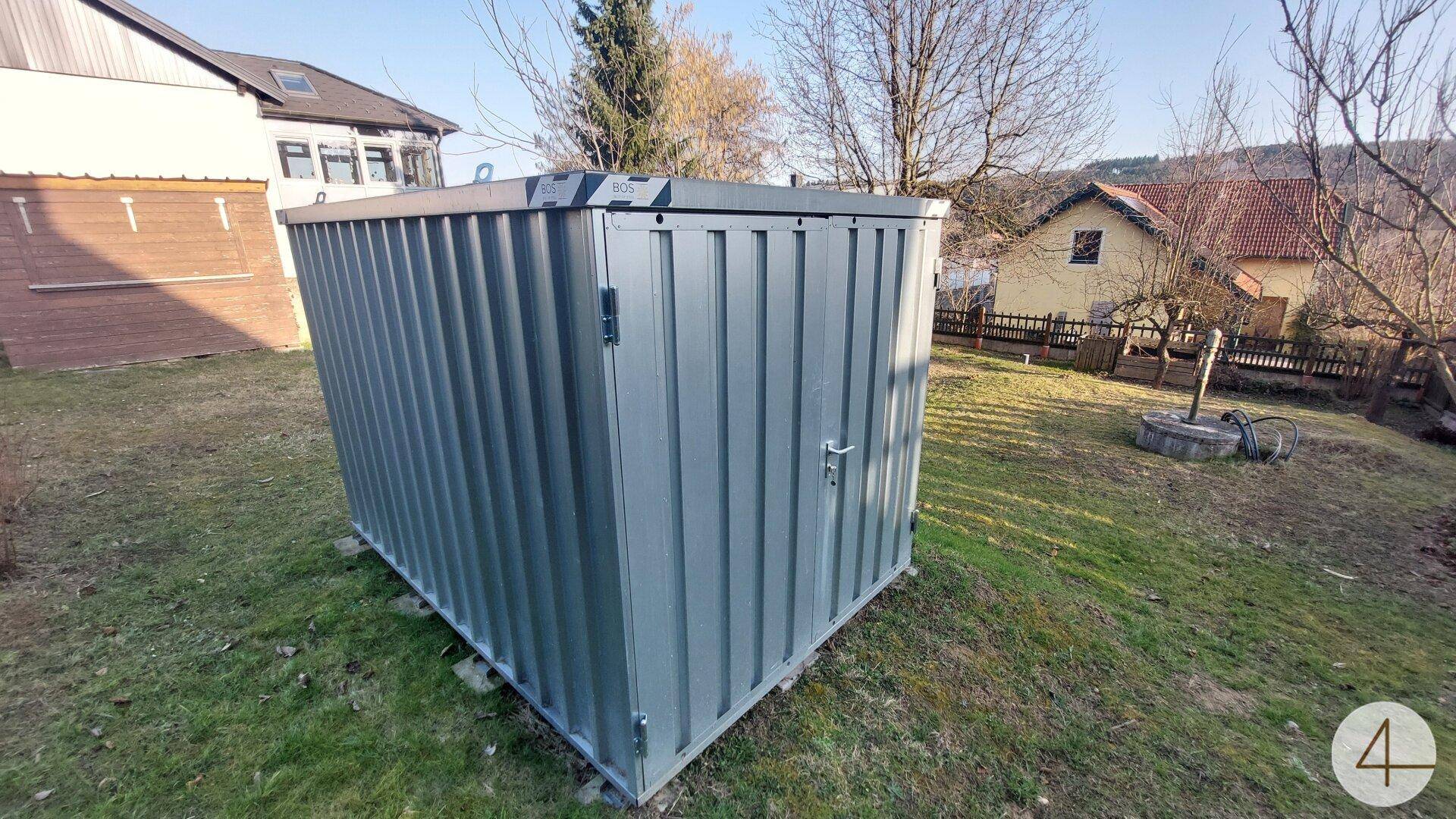 Moderner Metallschuppen im Garten, umgeben von Rasen und Bäumen, bietet praktischen Stauraum.