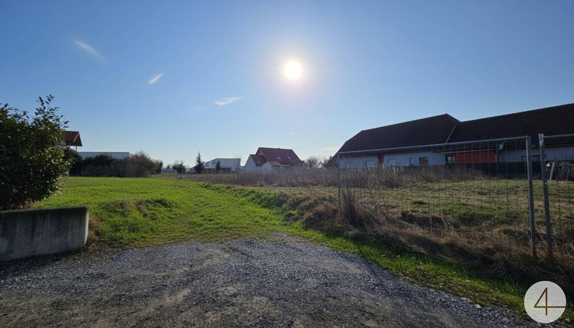 Sonniges Grundstück mit Schotterweg und Blick auf umliegende Gebäude unter klarem Himmel.