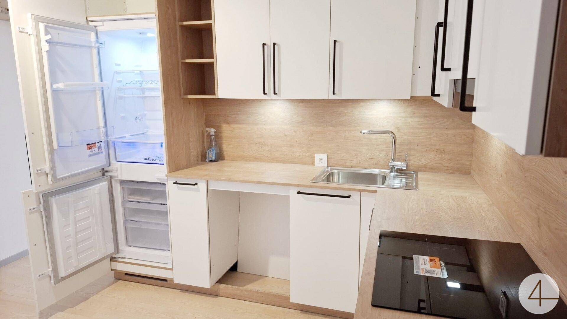 Moderne Küchenzeile mit weißen Schränken, Holzoptik-Arbeitsplatte und integriertem Kühlschrank.