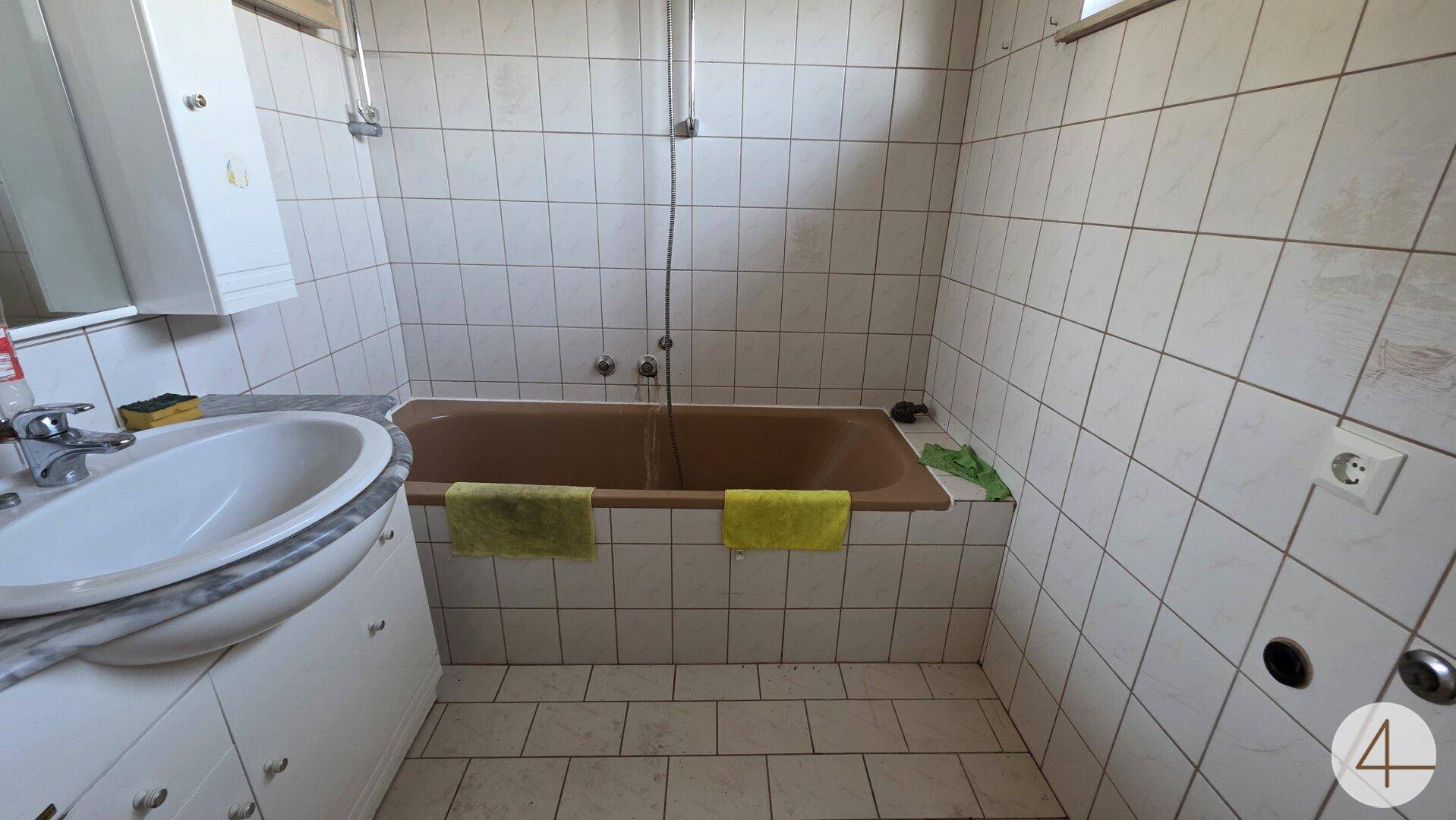 Badezimmer mit brauner Badewanne, weiß gefliesten Wänden und einem einzelnen Waschbecken.