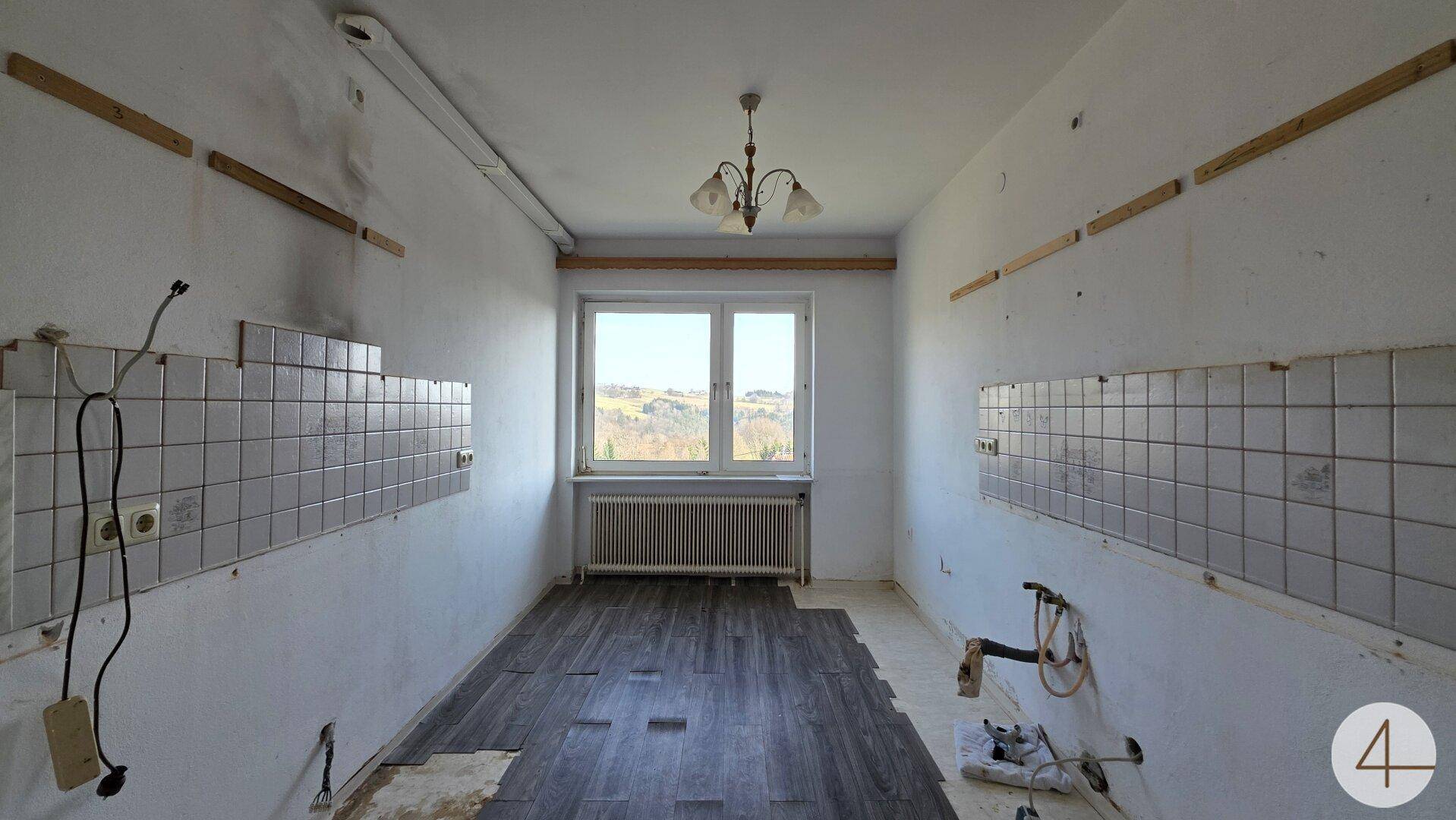 Leerer Küchenraum mit gefliesten Wänden, Laminatboden und Fenster mit Weitblick.
