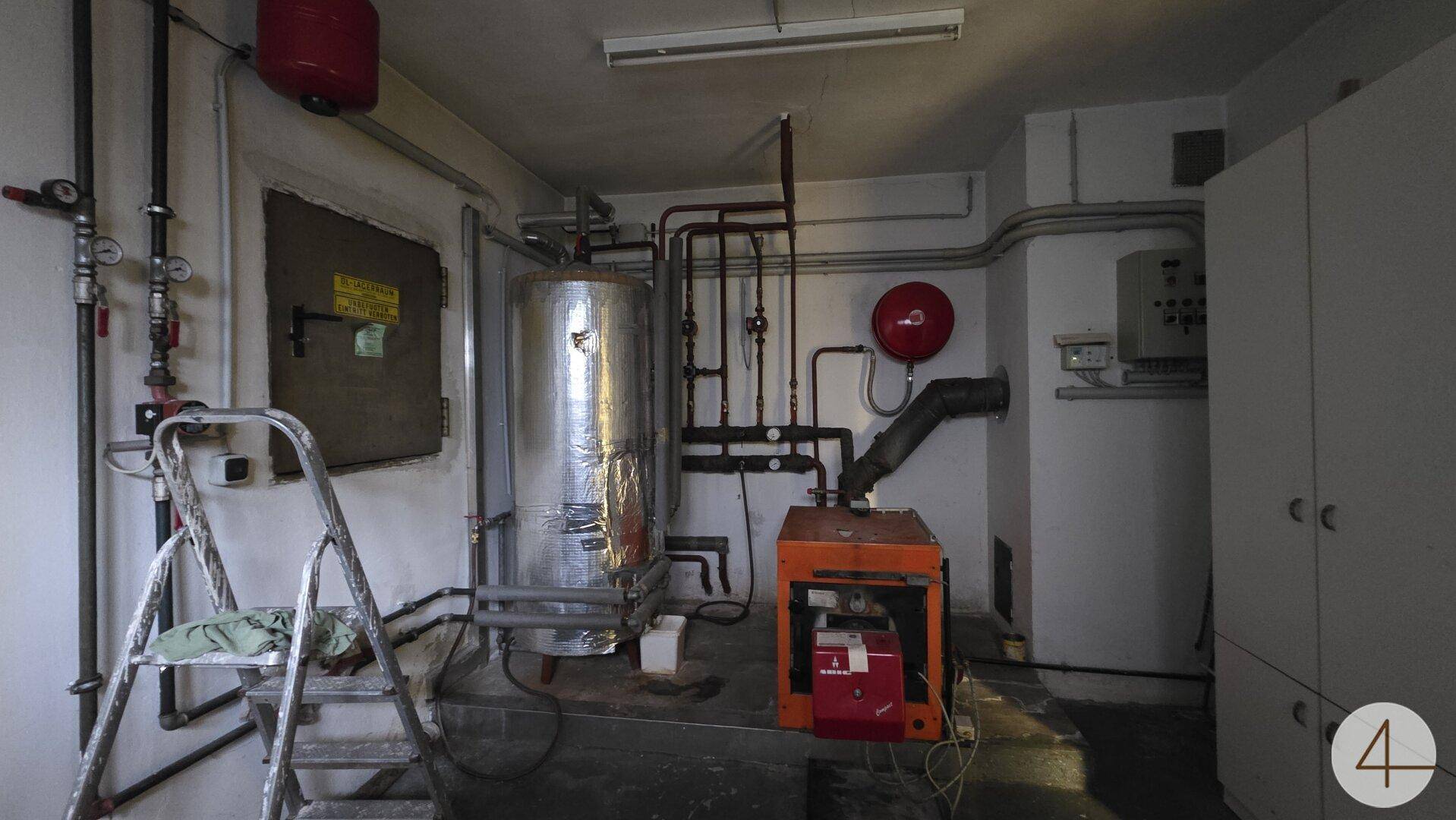 Heizungsraum im Keller mit Kessel, Rohren und Lagerregalen.
