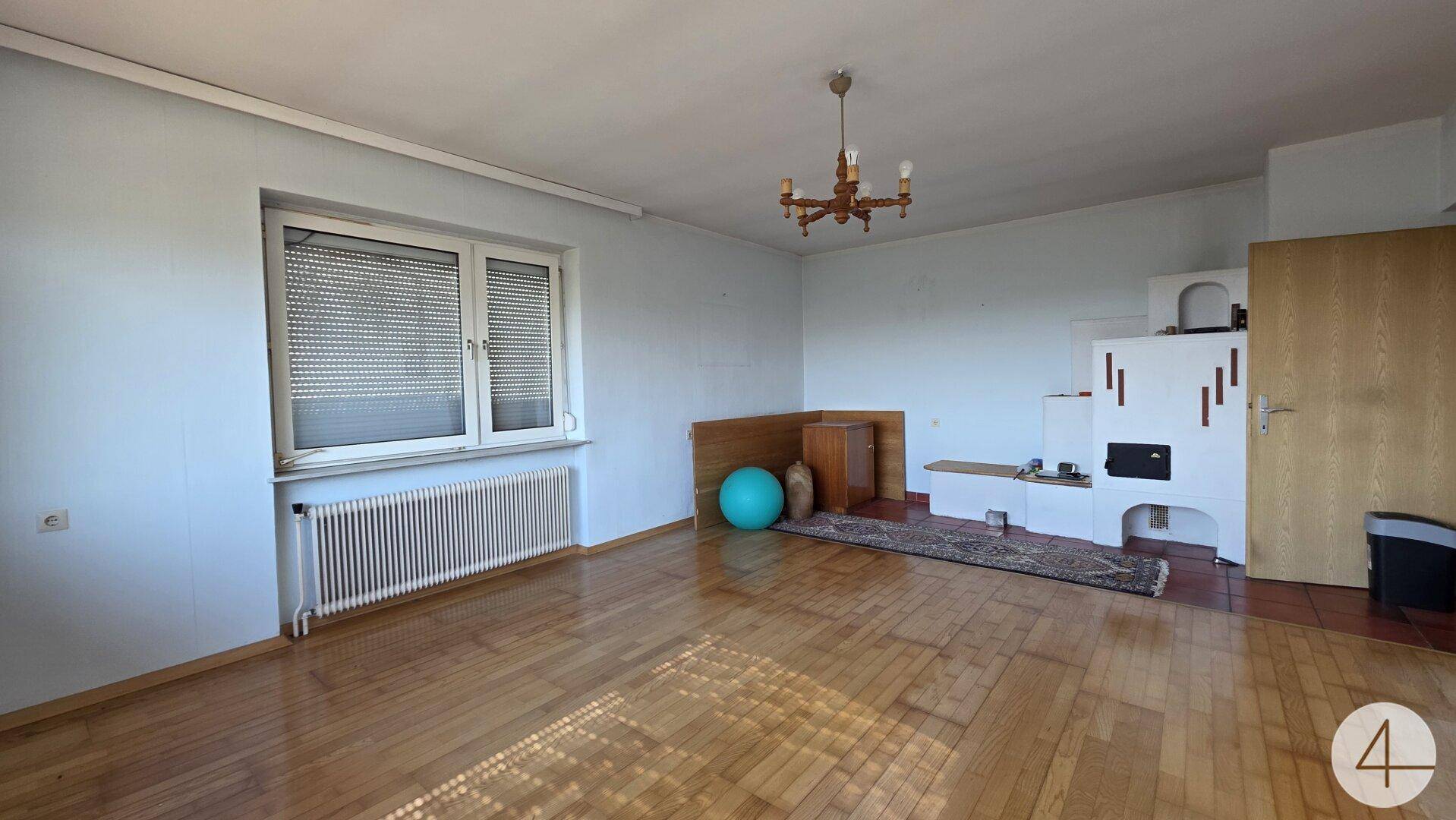 Geräumiges Wohnzimmer mit glänzendem Holzboden und einem traditionellen Kachelofen.