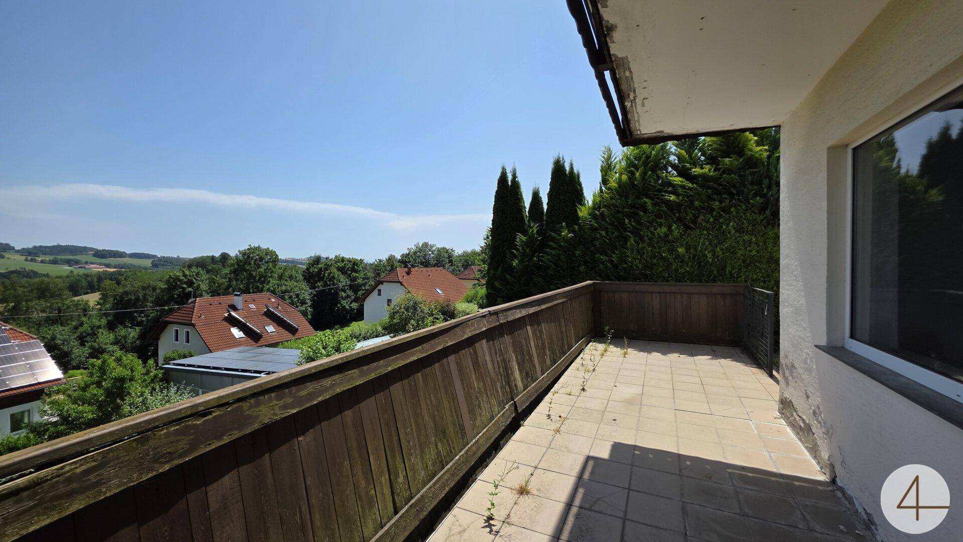 Balkon mit Fliesenboden und Holzgeländer, der eine weite Aussicht auf die Umgebung bietet.