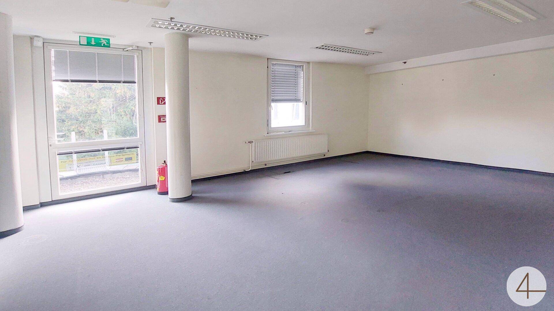 Geräumiger, leerer Bürobereich mit großem Fenster und Heizkörper, bereit zur individuellen Einrichtung.