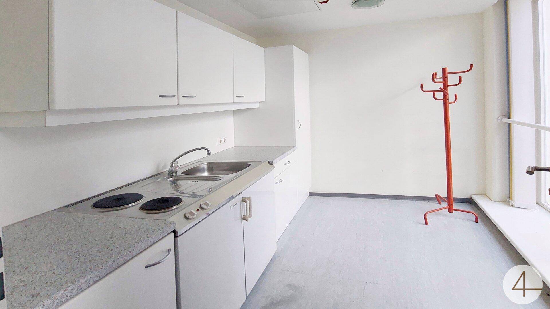 Funktionale Küchenzeile mit weißen Schränken, Spüle und Kochplatten, ideal für Pausen.
