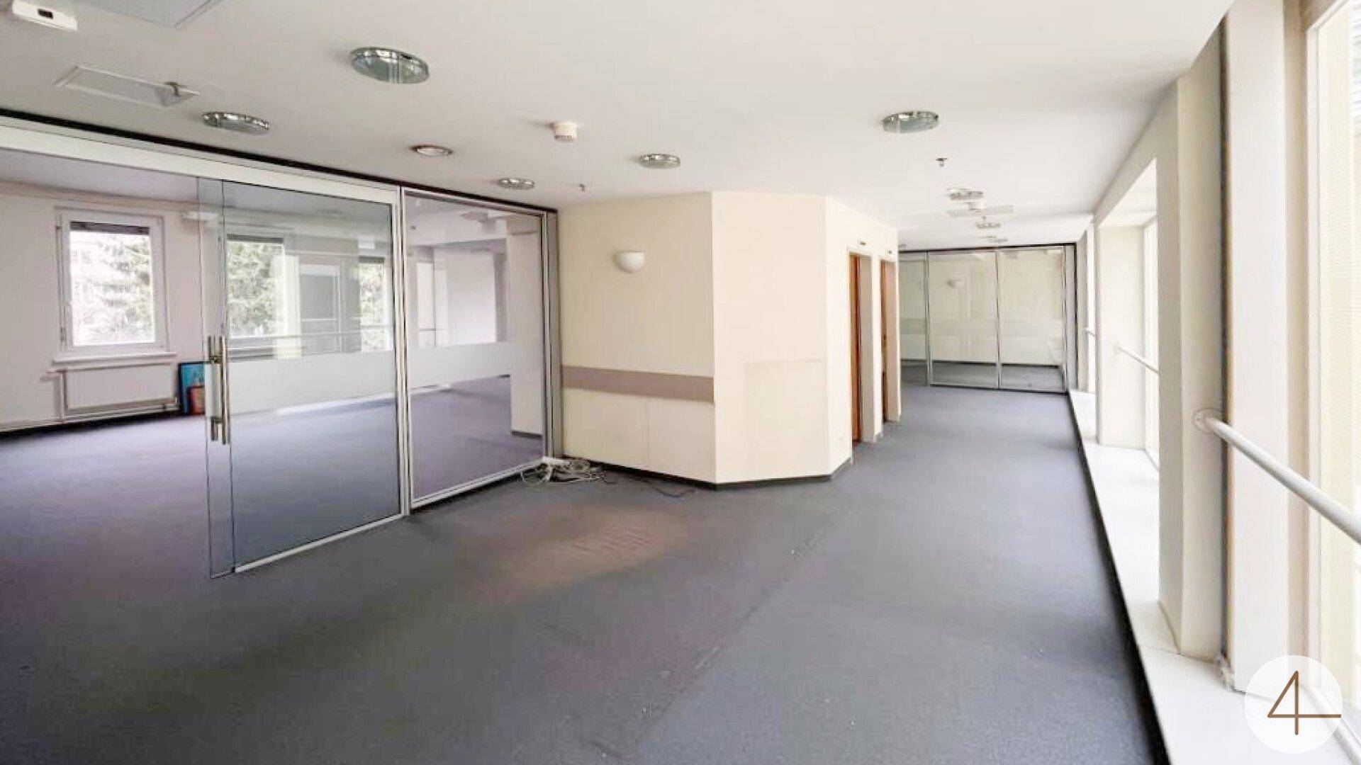Langer Bürogang mit Glaswänden, Fenstern und einem Aufzug, der zu weiteren Bereichen führt.