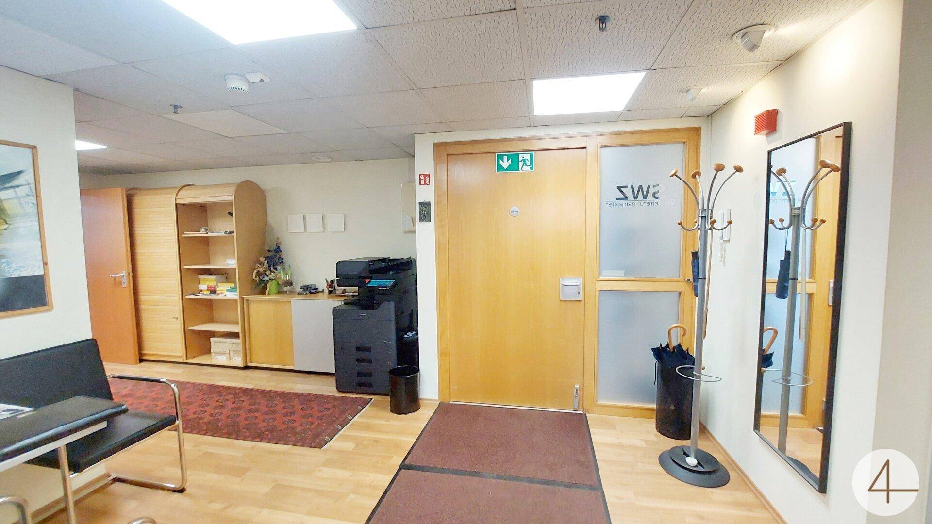 Empfangsbereich mit Holzboden, Garderobe und Zugang zu Büroräumen, hell und einladend.