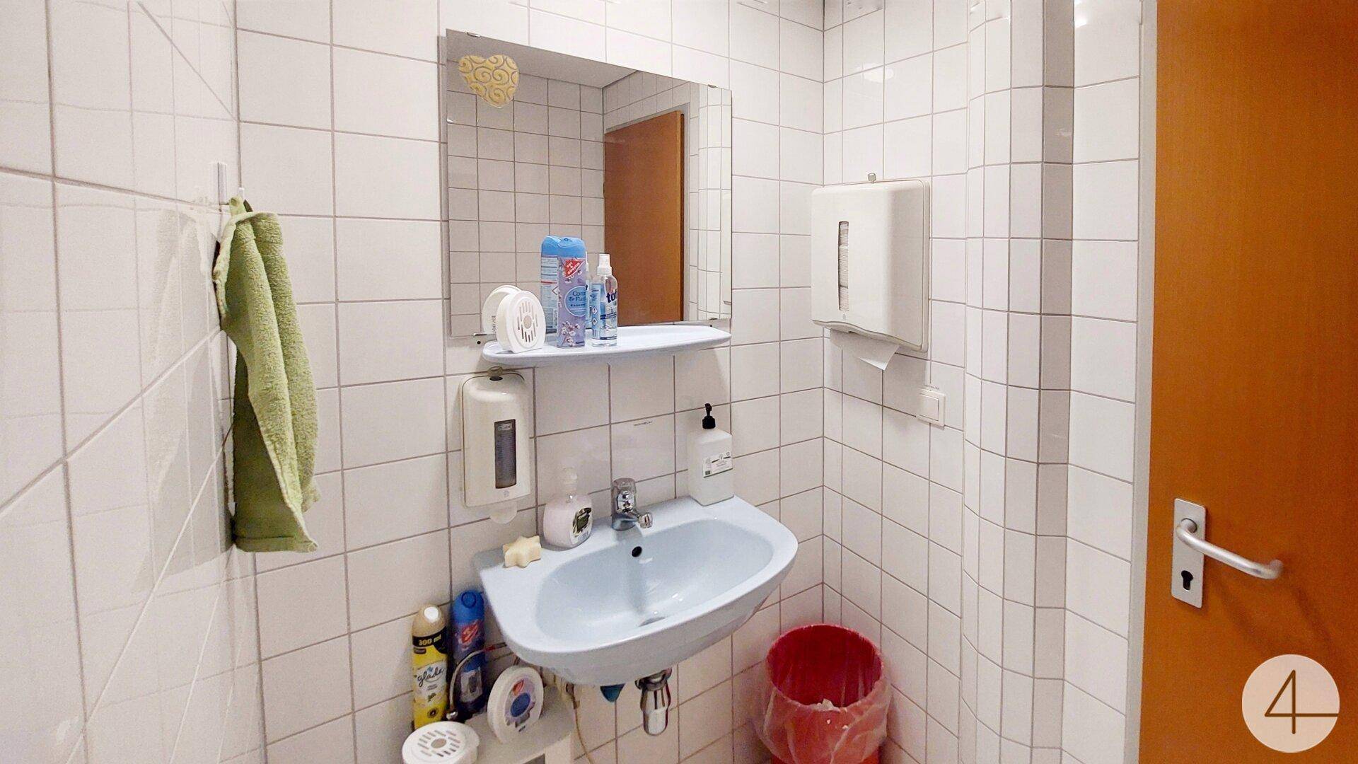 Kleines Badezimmer mit Waschbecken, Spiegel und weißen Fliesen, funktional und sauber.