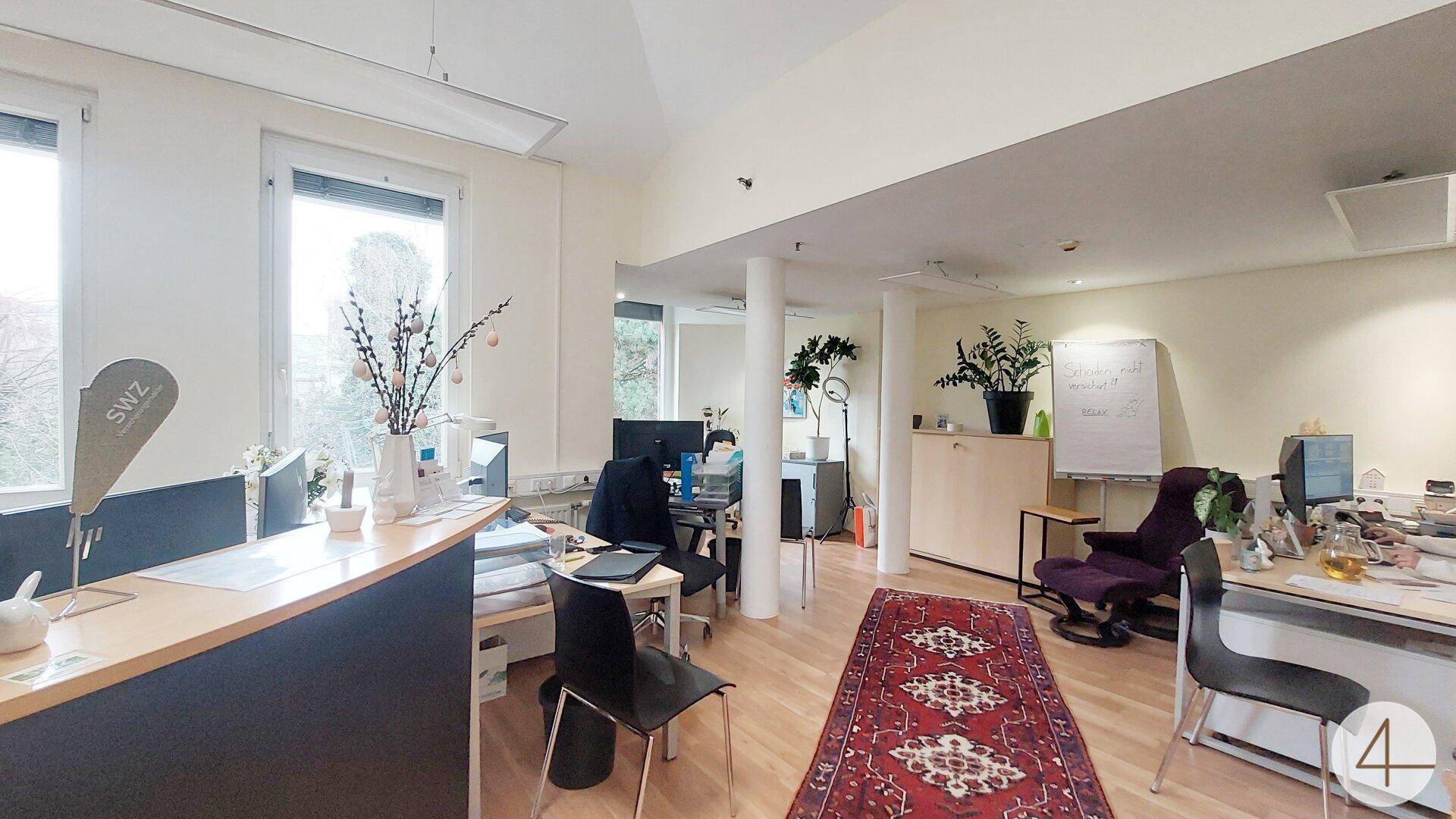 Großes offenes Büro mit mehreren Arbeitsplätzen, Holzboden und großen Fenstern mit Blick ins Grüne.