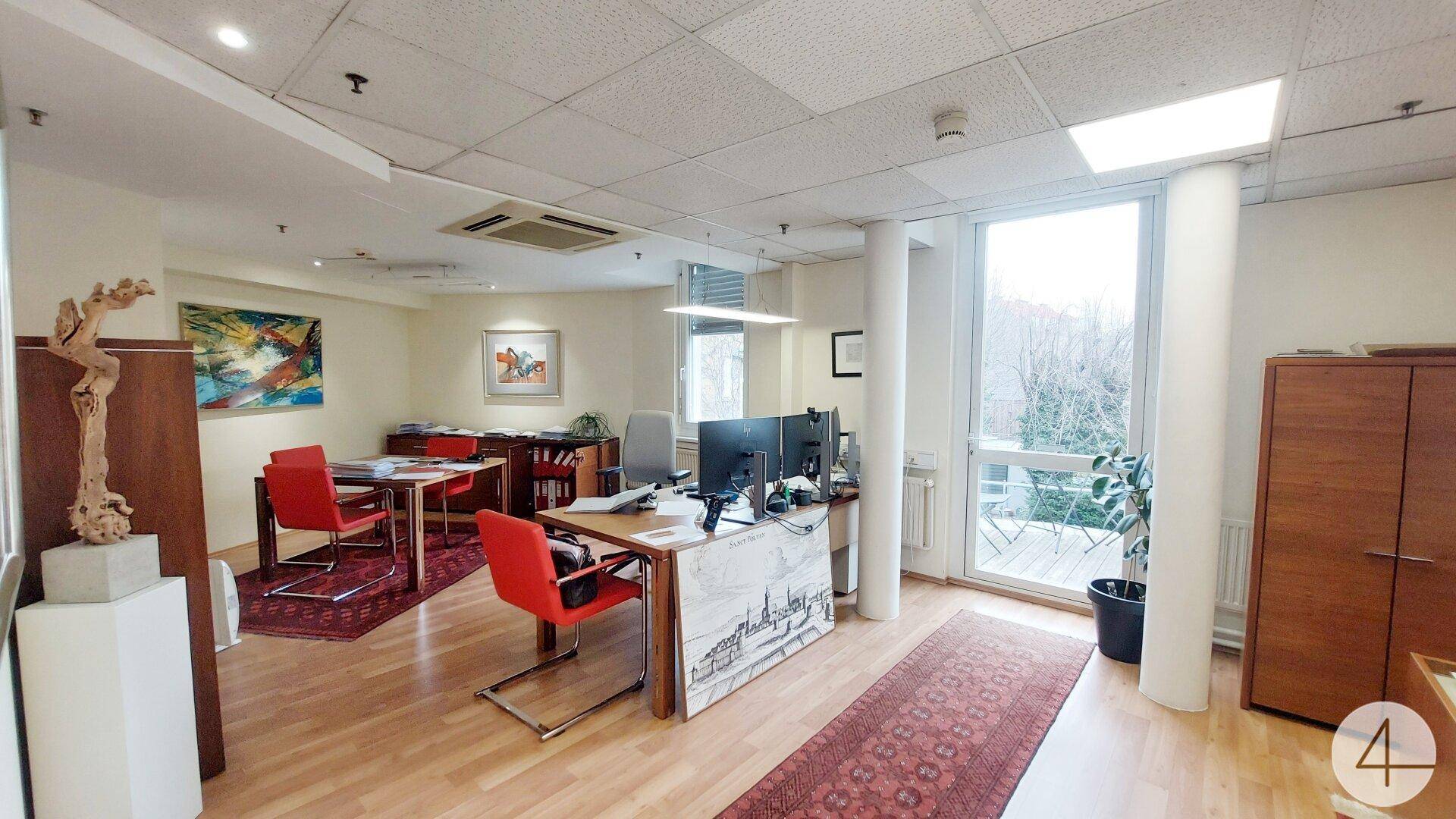Geräumiges Büro mit mehreren Arbeitsplätzen, Holzboden und Zugang zu einem Balkon oder Terrasse.
