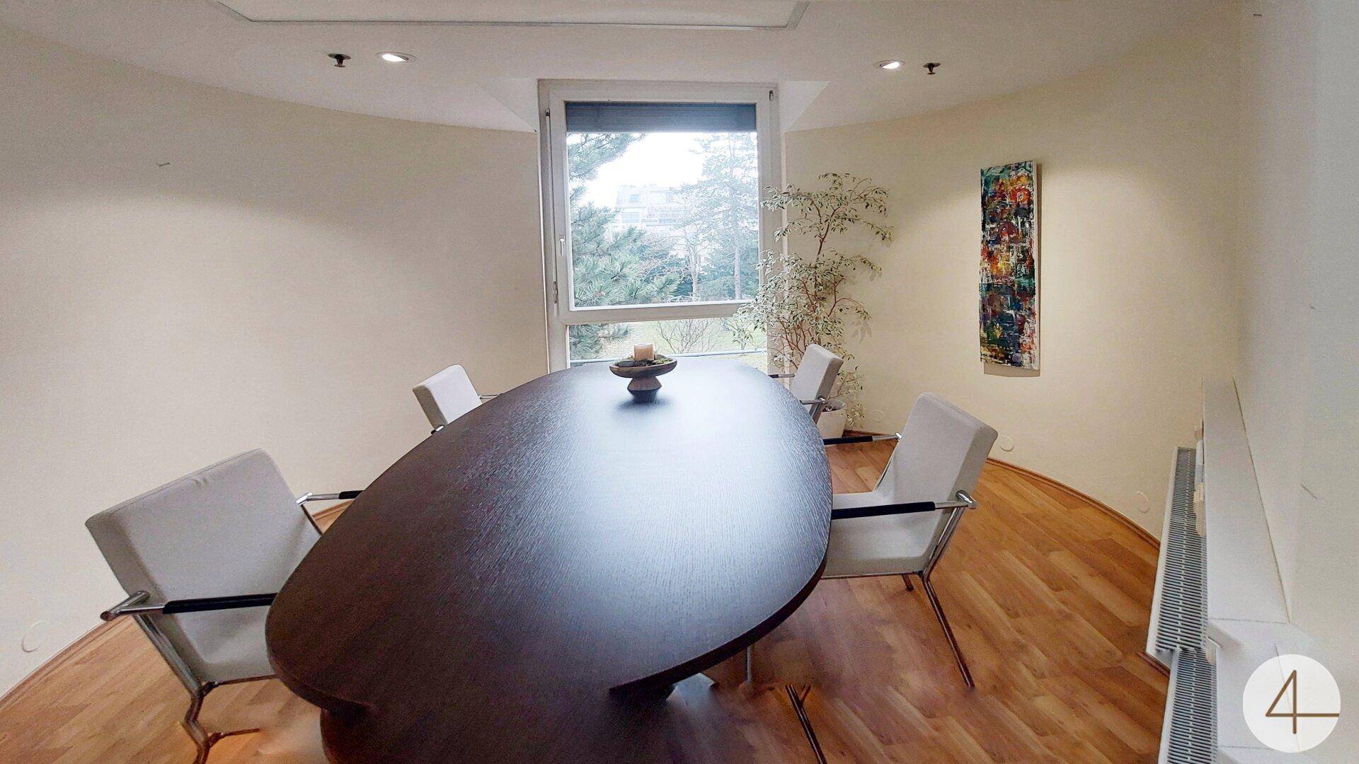 Moderner Konferenzraum mit ovalem Tisch, bequemen Stühlen und großem Fenster mit Ausblick.