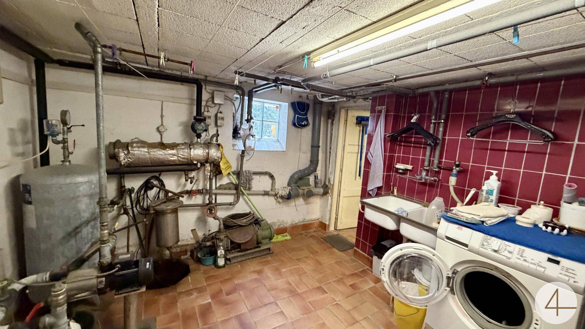 Hauswirtschaftsraum im Keller mit Waschmaschine, Spülbecken und Heizungsinstallationen.
