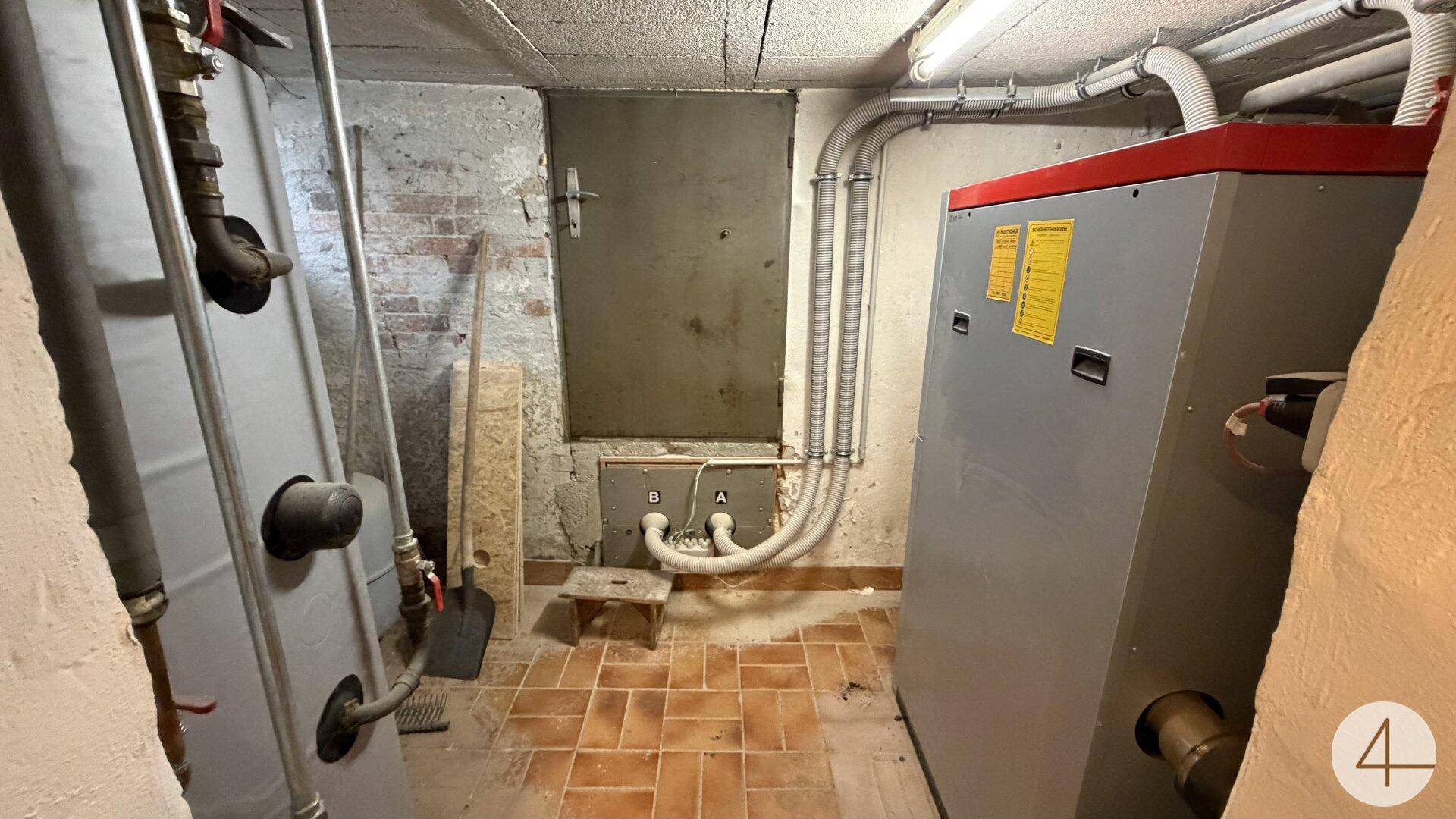 Heizungsraum im Keller mit großem Heizkessel und Rohrleitungen.