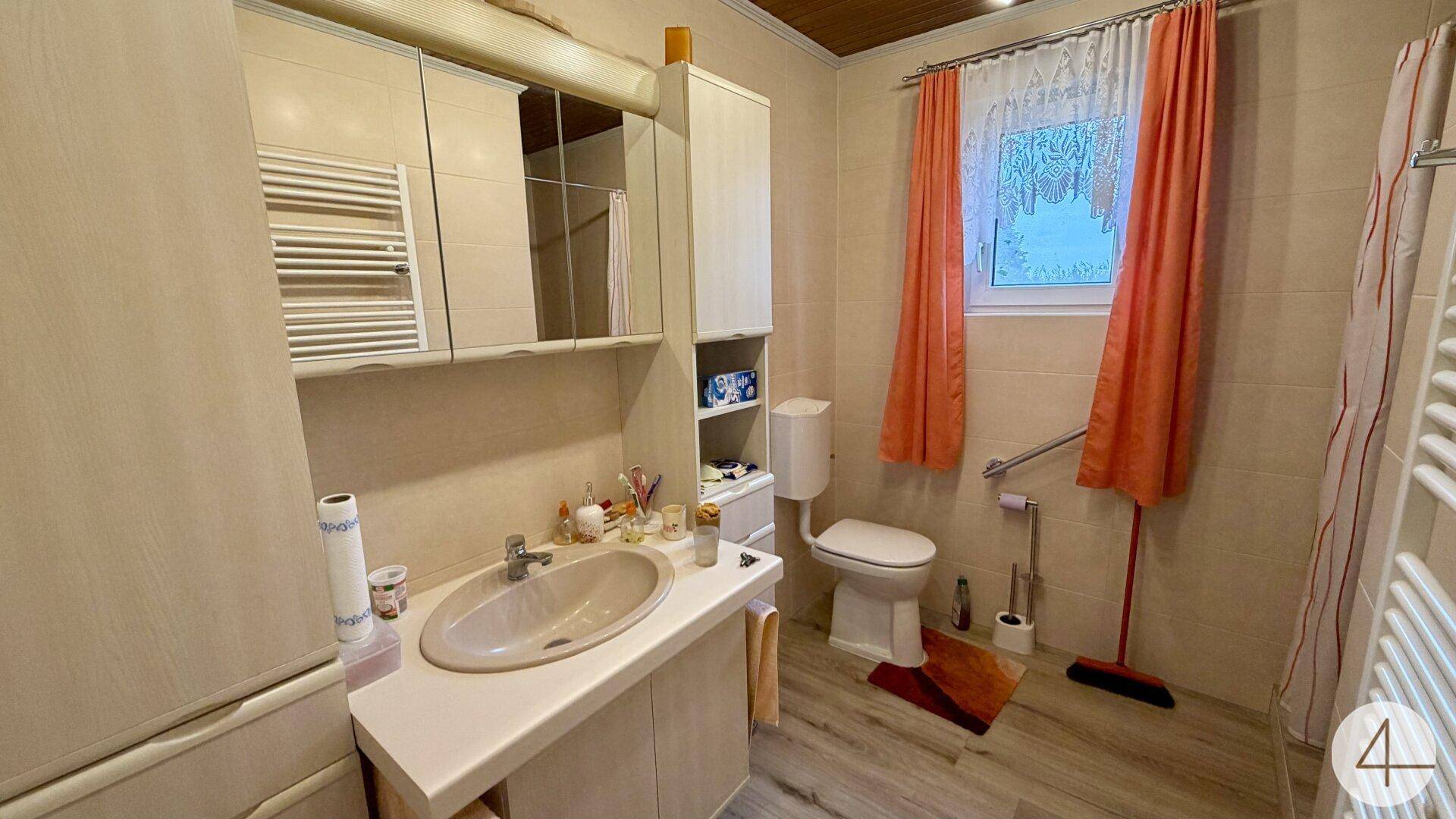 Badezimmer mit Waschbecken, Toilette, beheiztem Handtuchhalter und Haltegriffen.