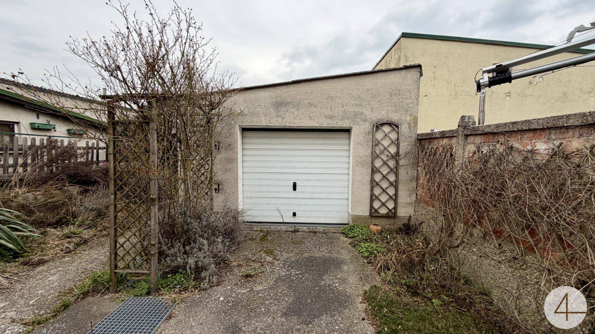Freistehende Garage im Hinterhofbereich mit weißem Rolltor.