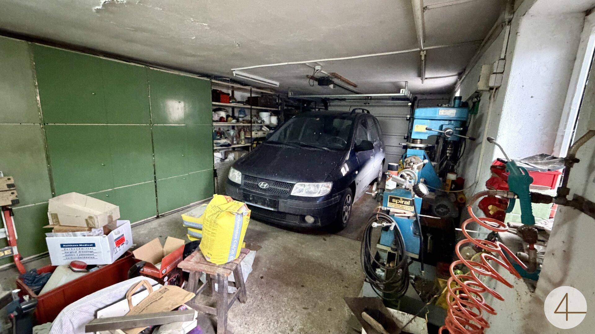 Innenansicht einer Garage mit geparktem Auto und Werkstattbereich.