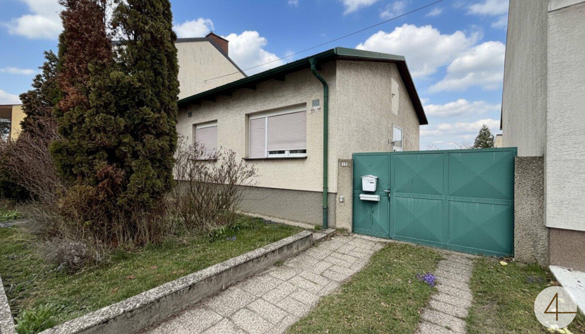 Ansicht eines älteren Einfamilienhauses mit grünem Tor und gepflasterter Einfahrt.