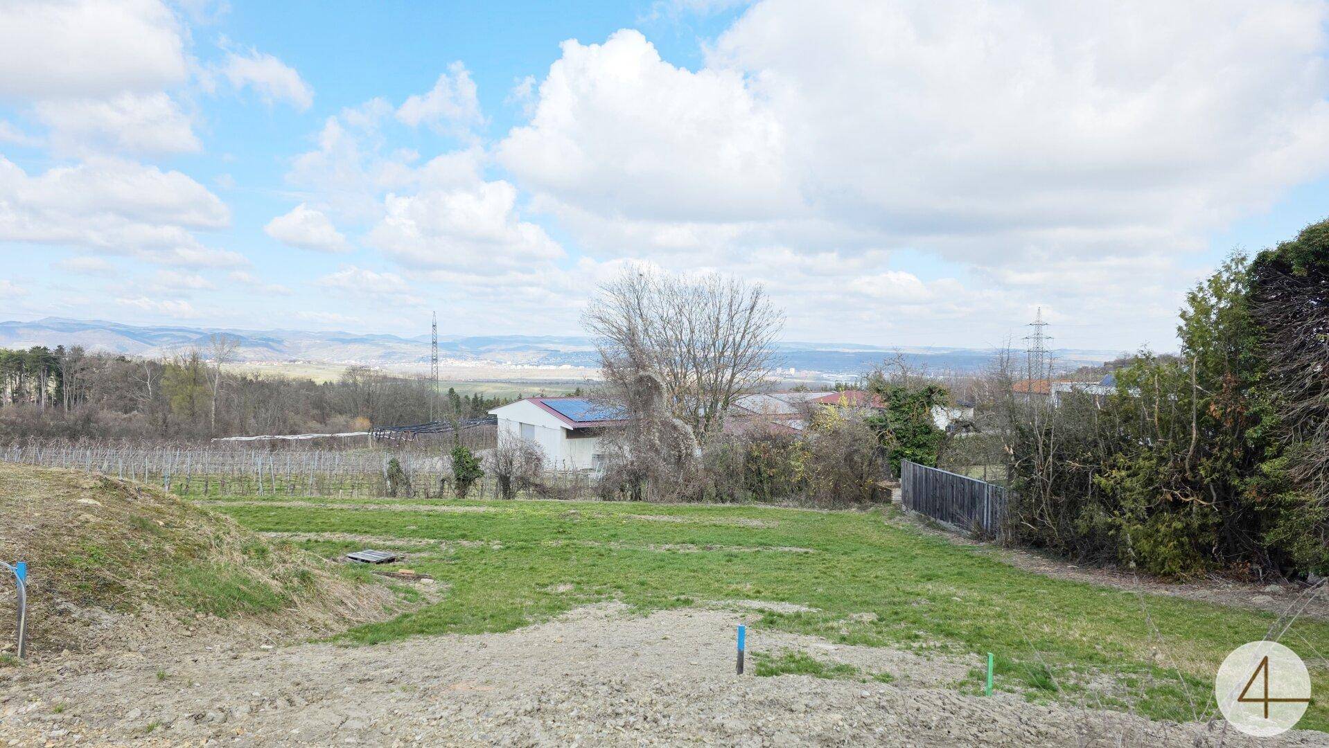 Offenes Grundstück mit Blick auf Weinberge und vereinzelte Häuser in der Ferne unter einem weiten Himmel.