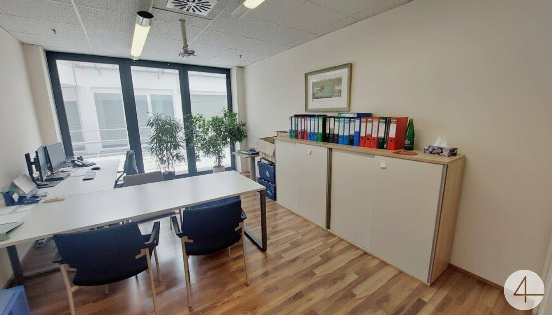 Büro mit Arbeitsplätzen, Blick auf den Innenhof und einem niedrigen Sideboard mit Aktenordnern.