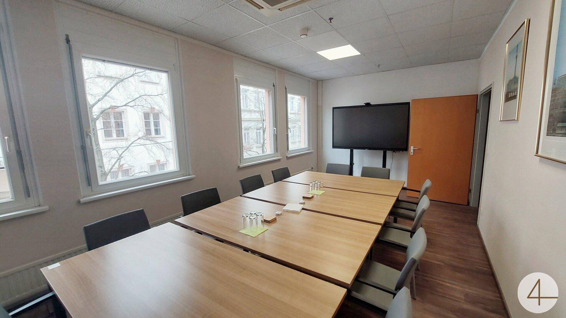 Besprechungsraum mit einem langen Holztisch, bequemen Stühlen und einem großen Bildschirm für Präsentationen.