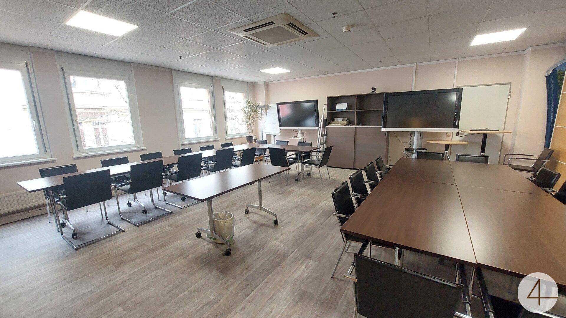 Geräumiger Konferenzraum mit flexiblen Tischen, modernen Bildschirmen und hellem Laminatboden.