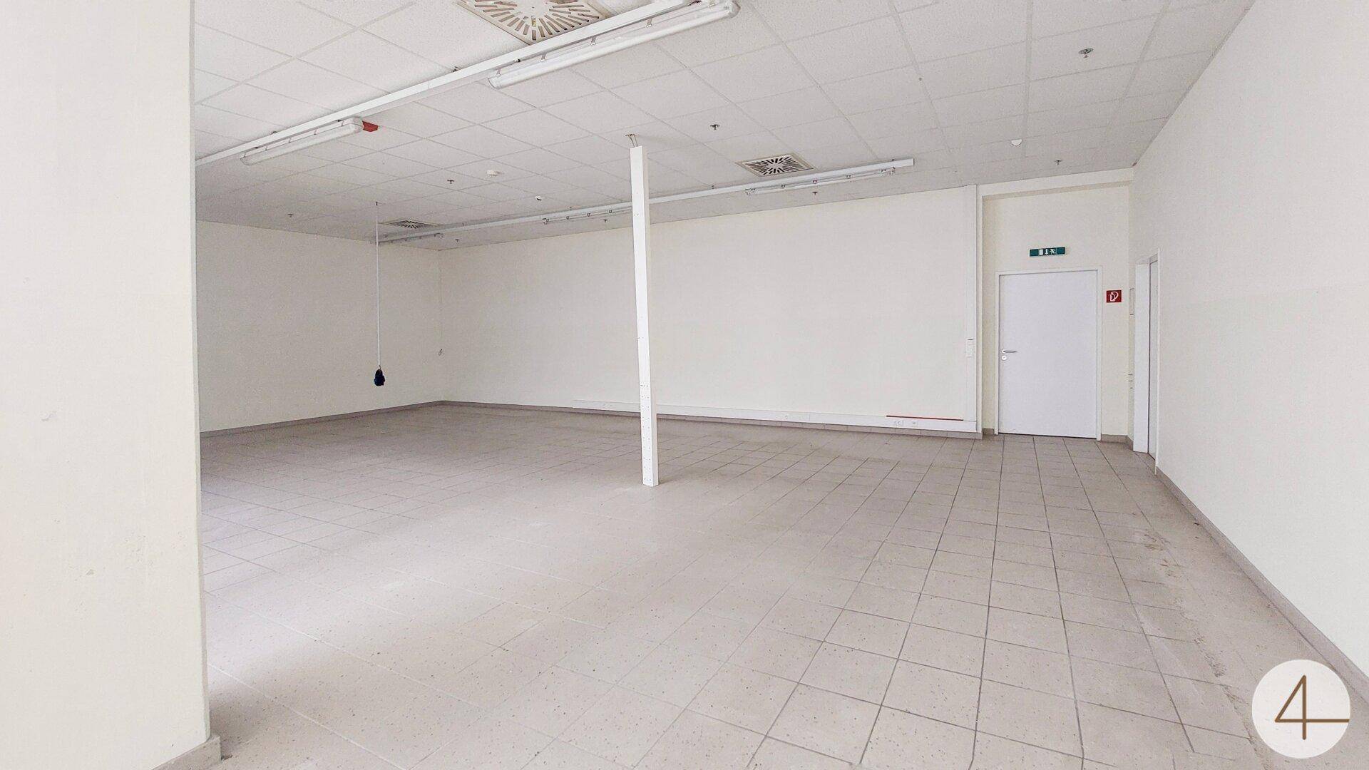 Heller, leerer Gewerberaum mit Fliesenboden und abgehängter Decke, bereit zur individuellen Gestaltung.