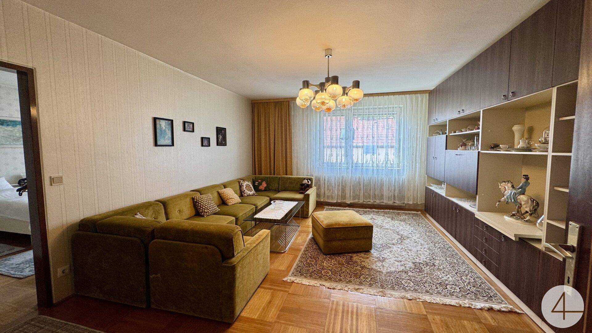Gemütliches Wohnzimmer mit großem Ecksofa, Parkettboden und einer Schrankwand mit Dekorationen.