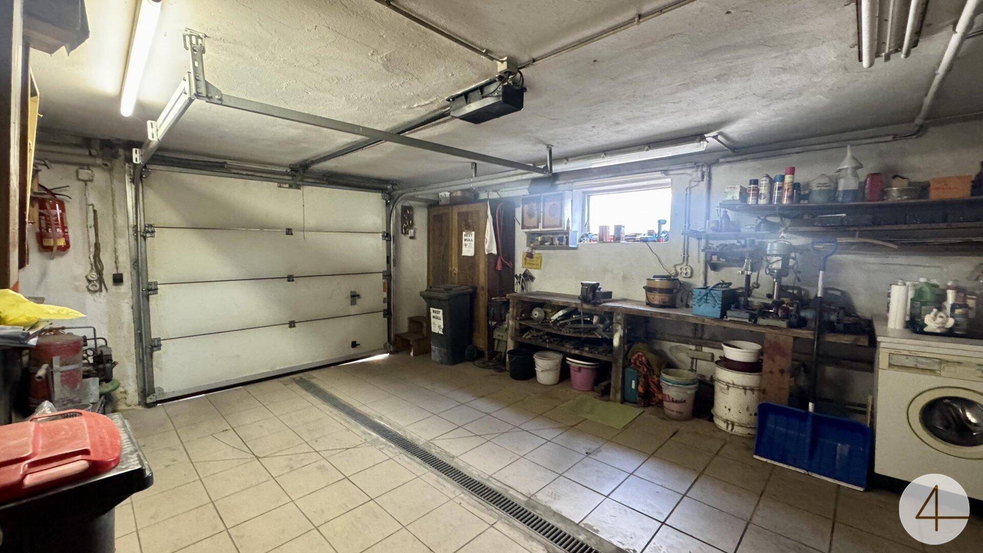 Geräumige Garage mit Werkbank, Fliesenboden und Waschmaschine, ideal als Hobbyraum.