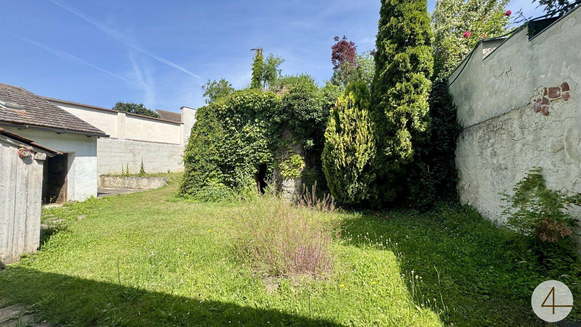 Grüner Gartenbereich mit Rasenfläche und einer alten, mit Efeu bewachsenen Steinmauer.
