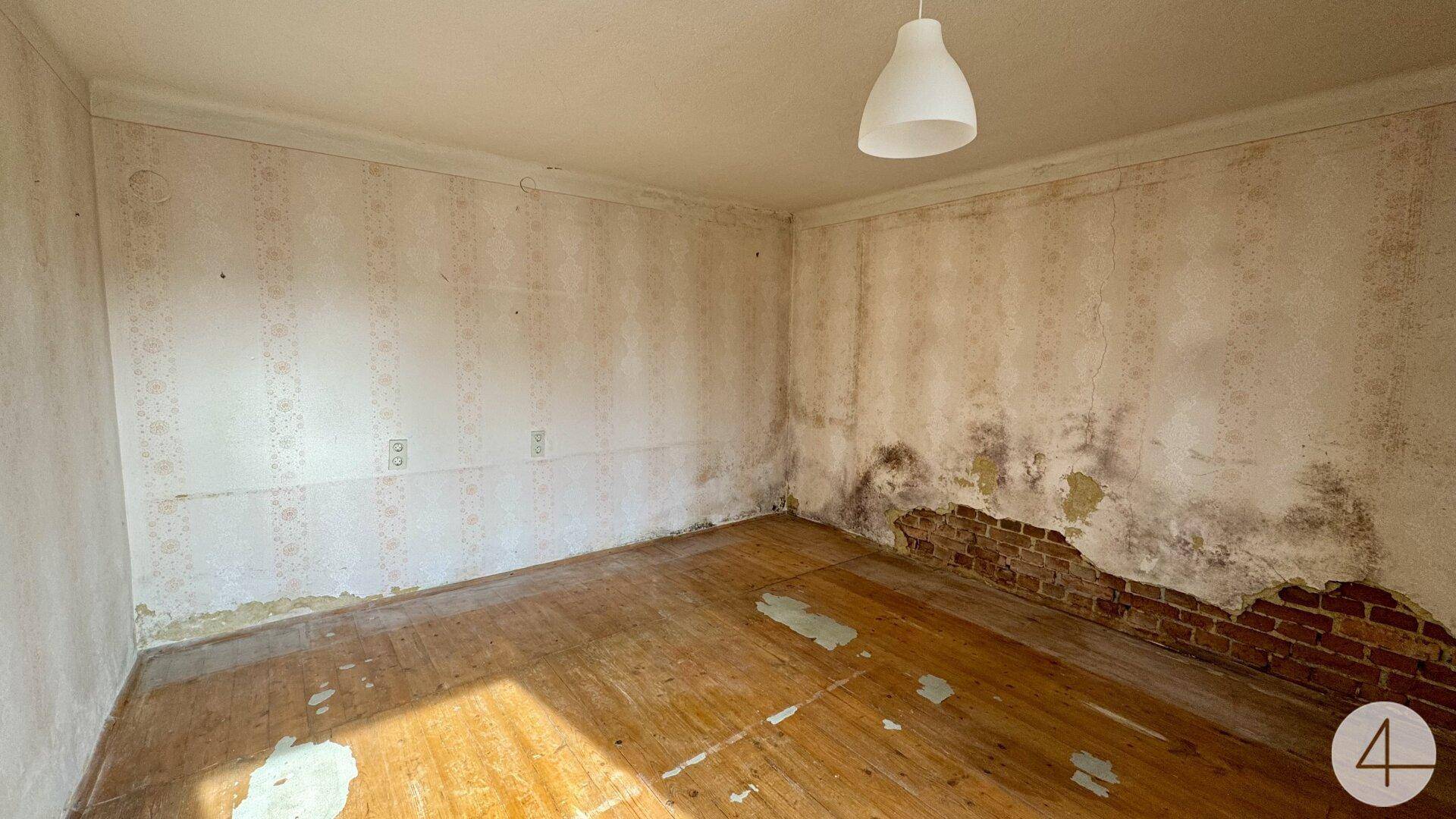 Leerer Raum mit beschädigten Wänden und abgenutztem Holzboden, der eine Renovierung benötigt.